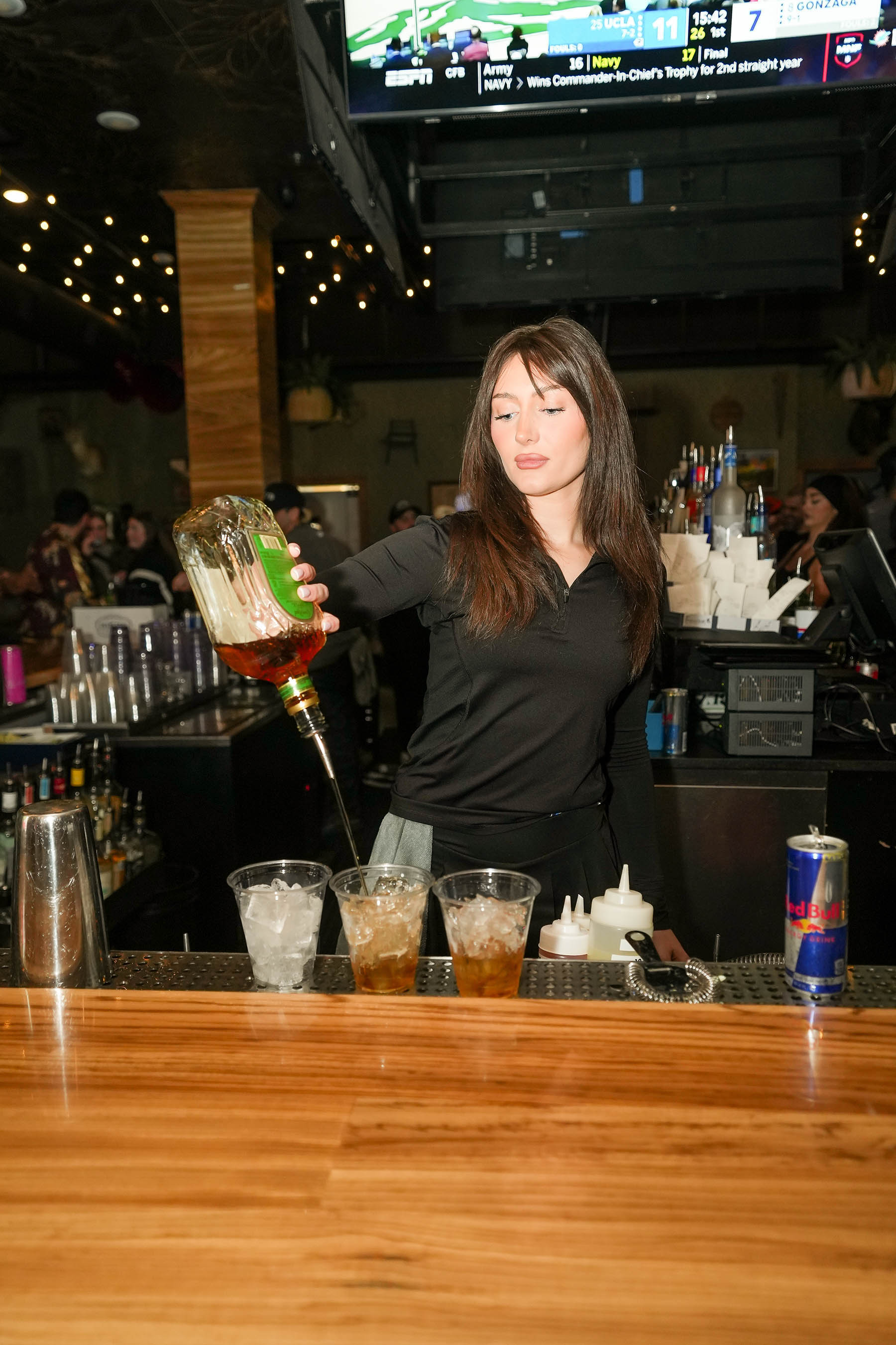 A bartender pouring at the bar at BLVD Park in Houston Heights, bottles and taps behind and an ESPN scoreboard on the screen above